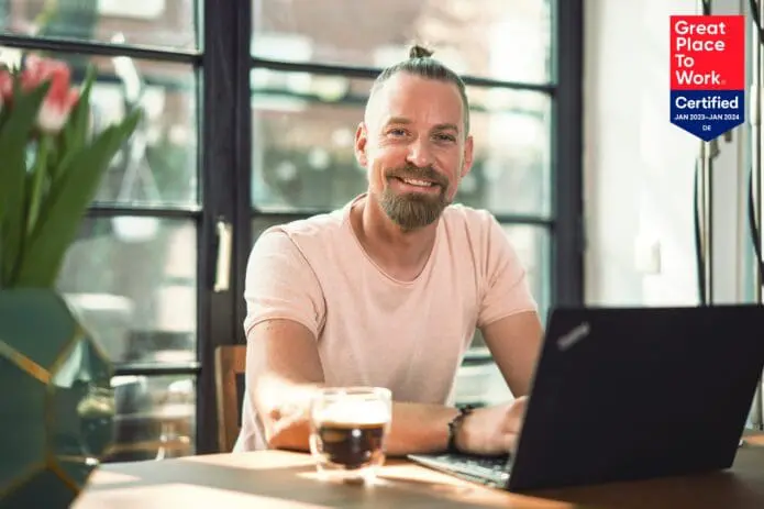 Professor sitzt mit Kaffee im Home Office und Great Place to Work Logo