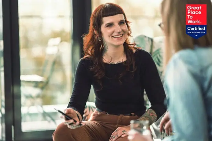Jana zeigt Amira etwas am Handy und Great Place to Work Logo