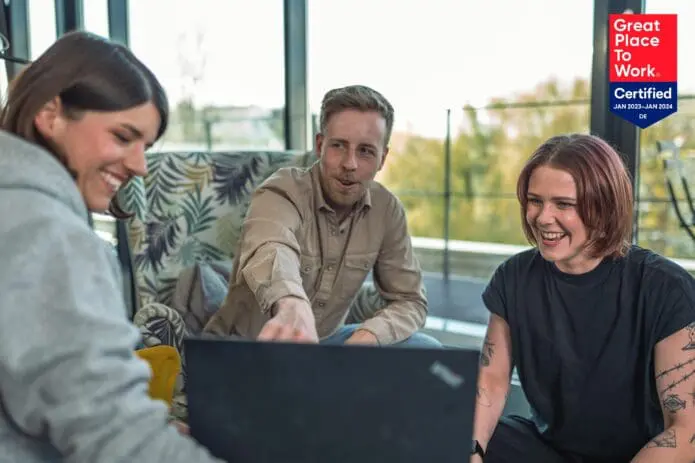Drei Kollegen zeigen sich etwas am Laptop und Great Place to Work Logo
