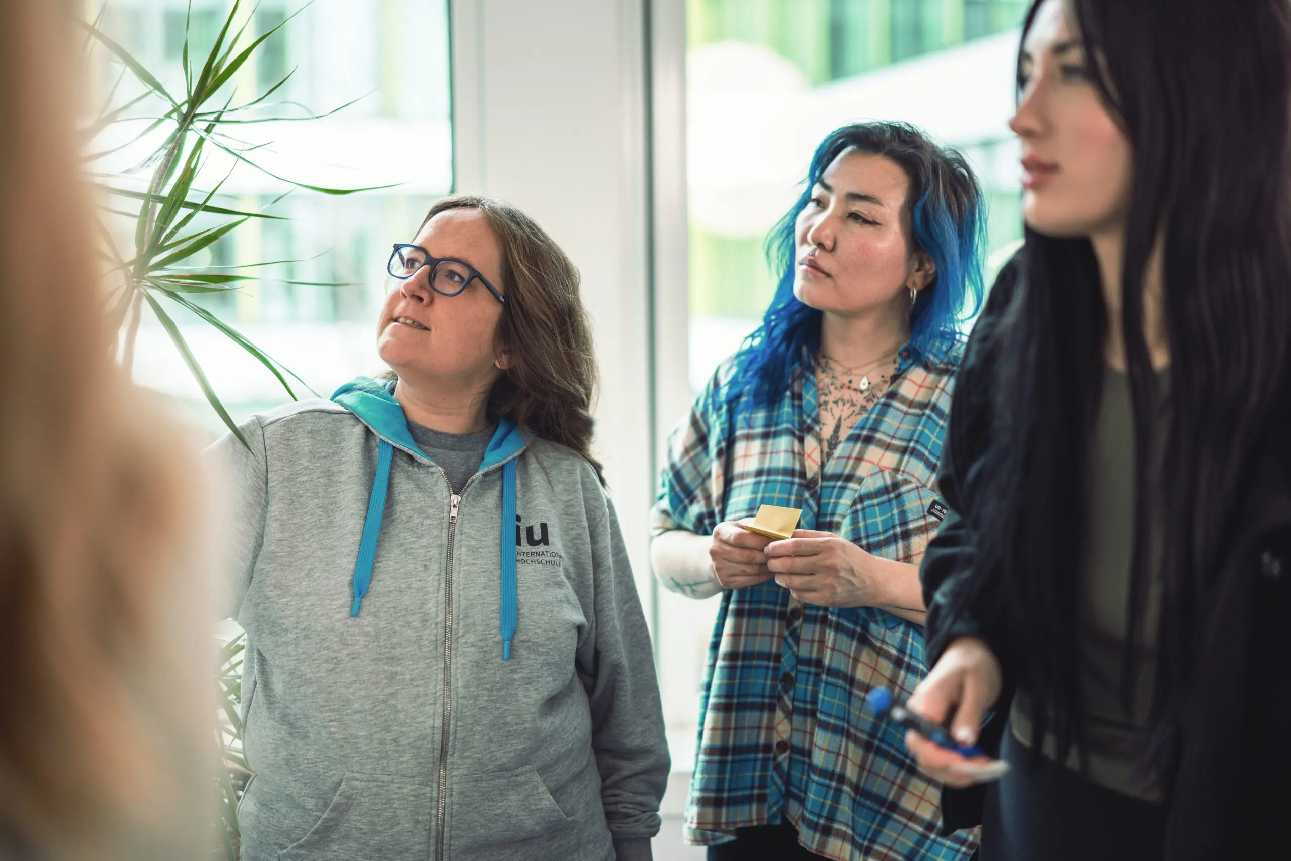 Dozentin im IU-Pullover erklärt ihren Studentinnen etwas an der Tafel