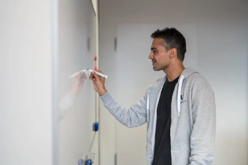 Man writing on whitaboard wall smiling from tech department