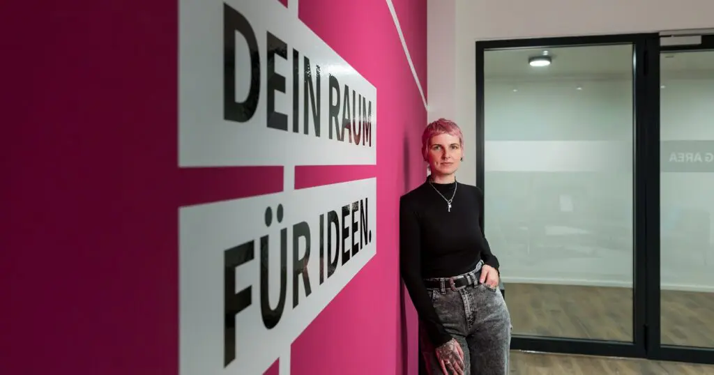 Frau mit rosa Haaren steht vor einer pinken Wand