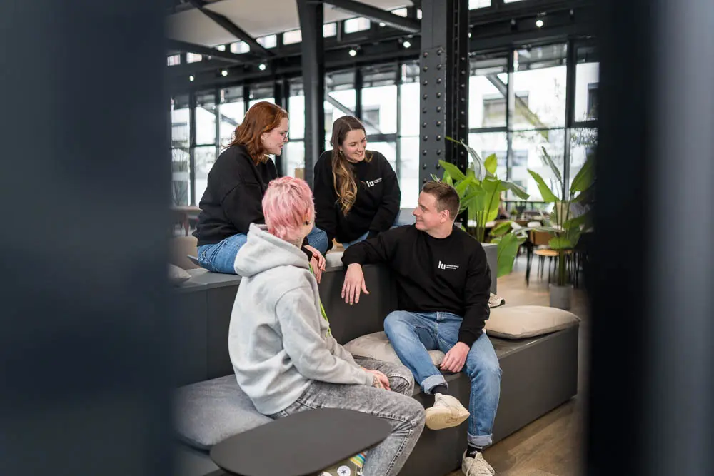 Lockeres Gespräch am Campus: Drei Frauen und ein Mann sitzen zusammen auf den Treppenstufen