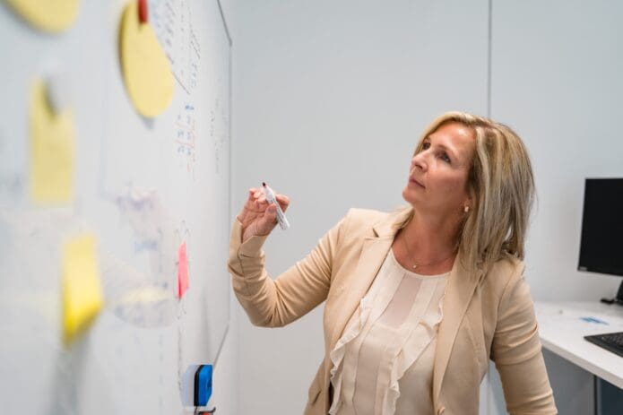 Dozentin schreibt ans Whiteboard und sieht nachdenklich aus